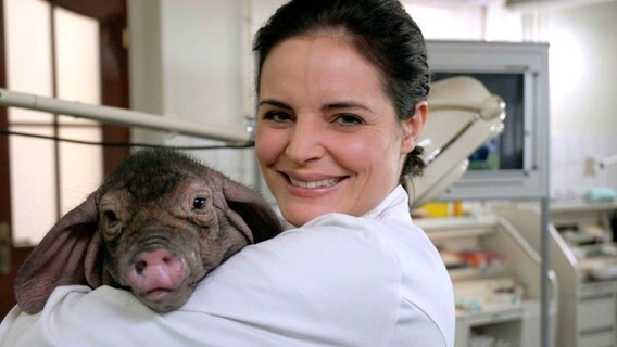 Eine Frau steht in einer Tierarztpraxis und hat ein kleines Schwein auf dem Arm. © ARD/Christa Köfer Foto: Christa Köfer