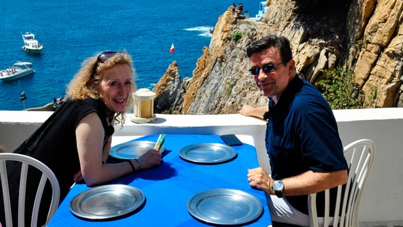 Kreuzfahrtdirektor Thomas Gleiß und Entertainerin Kiona auf der Terasse des La Perla mit Blick auf die Felsenspringer von Acapulco, Mexiko. © Bewegte Zeiten GmbH/Christian Hattesen 