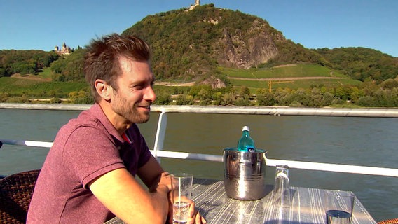 Vom Rheinschiff aus hat Moderator Daniel Aßmann eine ganz andere Perspektive auf den Drachenfels und die Weinberge. © WDR 