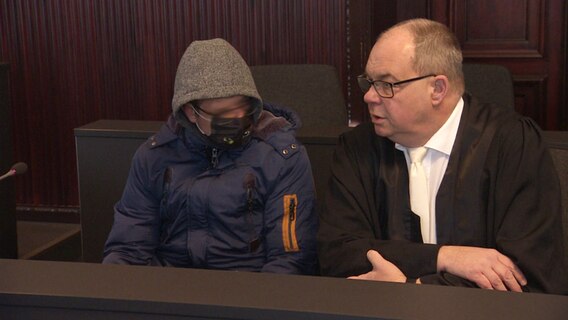 Der Angeklagte in einem Missbrauchs-Prozess sitzt im Schweriner Landgericht neben seinem Verteidiger. © Screenshot 