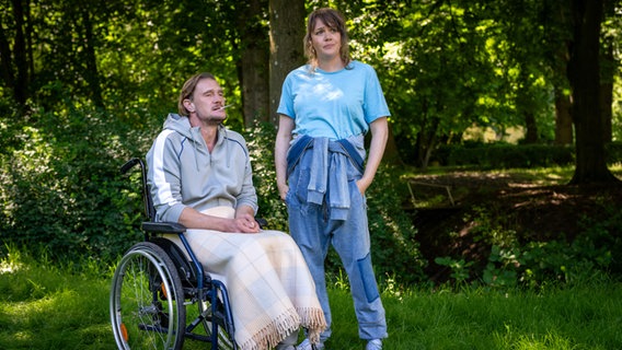 Szenenbild aus der NDR Serie "Reisen mit Muddi": Ein Mann sitzt im Rollstuhl, eine Frau steht daneben. © NDR/Boris Laewen Foto: Boris Laewen