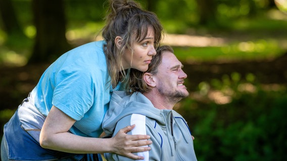 Szenenbild aus der NDR Serie "Reisen mit Muddi": Ein Mann sitzt im Rollstuhl, eine Frau beugt sich von hinten über ihn. © NDR/Boris Laewen Foto: Boris Laewen