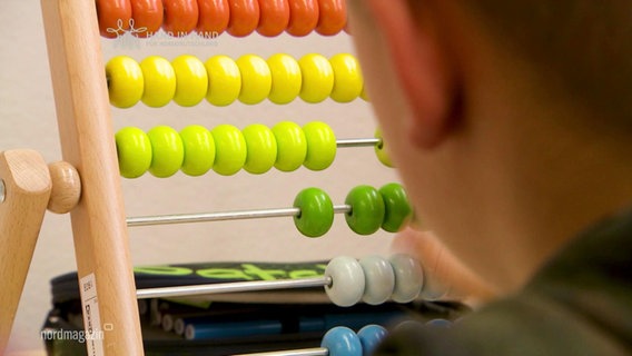 An abacus for practicing arithmetic problems, a child's head blurred in the cut.  