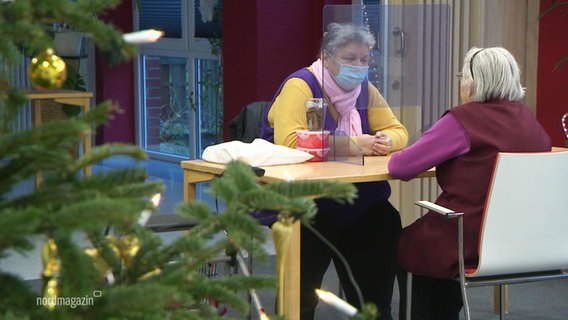 Two people in the old people's home, separated by a protective glass.  