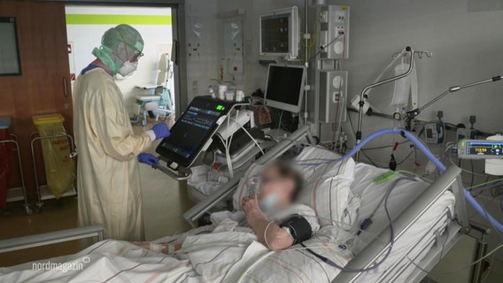 A woman is lying in a hospital bed.  Next to her is a person in protective clothing.  