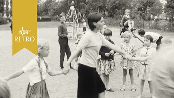 Erzieherin beim Ringelreigen mit Kindern auf einem Spielplatz 1965  