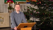 Pastor Jonas Goebel at the pulpit.  Behind him is a decorated Christmas tree.  