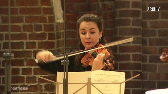 A woman plays the violin with a music stand in front of her.  