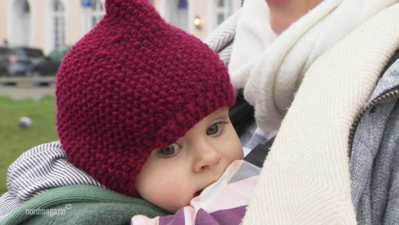 A small child with a hat on its mother's arm.  