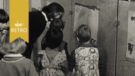 Kinder in einer Malschule mit Erzieherin beim Betrachten ihrer Bilder an der Wand (1965)  