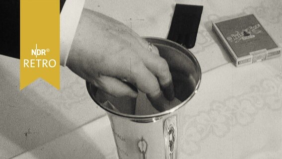 Hand greift in einen Pokal, um ein Los herauszuziehen (1965)  
