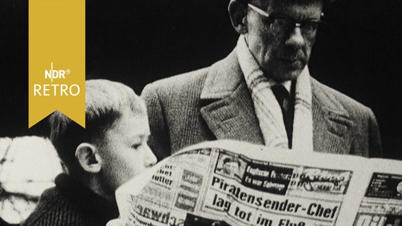 Foto von zeitunglesendem Mann mit einem Kind, das mit hineinguckt (1965)  