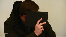 Der Angeklagte im Gerichtssaal versteckt sein Gesicht hinter einem Tablet