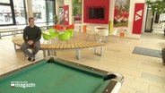 A man is sitting in an empty lobby of a youth hostel.  