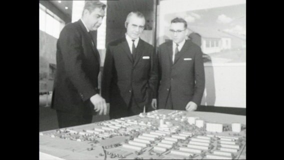 Teilnehmer einer Tagung stehen um ein das Modell einer Reihenhaussiedlung (1964)  