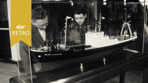 Vater und Sohn hinter einer Vitrine mit einem Schiffsmodell (1965=  
