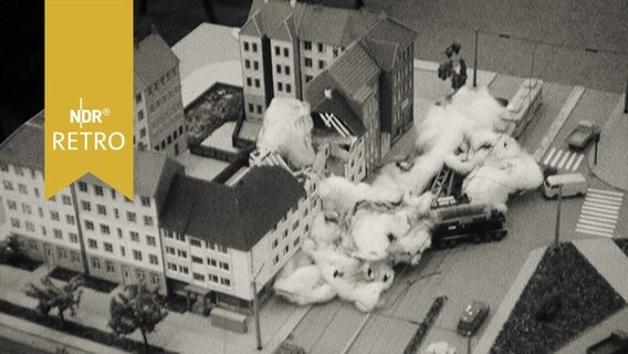 Modell mit Spielzeugautos und Häusern, das eine Wohnhausexplosion simuliert, die Rauchschwaden sind aus Watte (1964)  