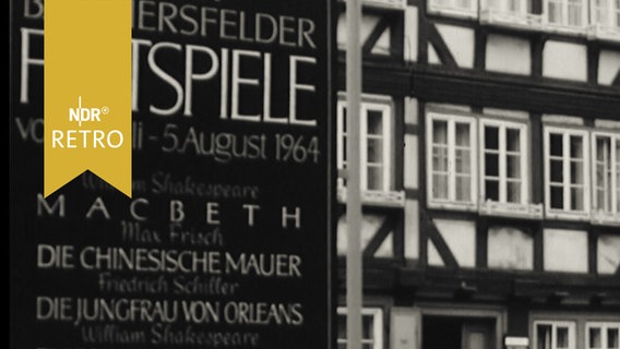 Ankündigungstafel "Bad Hersfelder Festspiele vom 3. Juli - 5. August 1964" in der Hersfelder Innenstadt neben einem Fachwerkhaus  