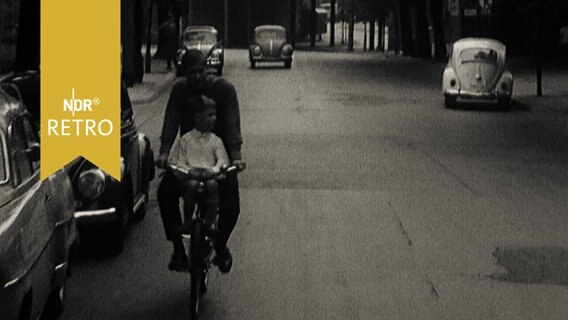 Vater mit Kind auf dem Vordersitz auf dem Fahrrad in einer Wohnstraße 1964  