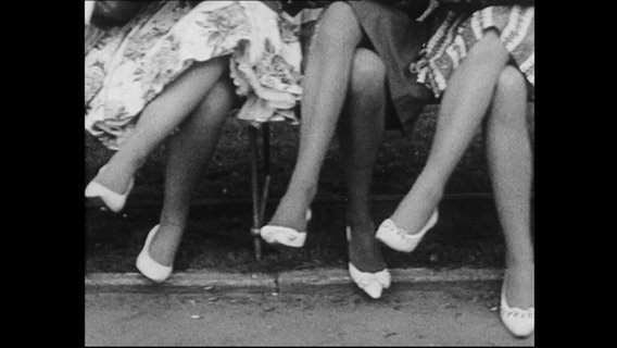 Drei Frauen sitzen auf einer Bank und überschlagen ihre Beine in die selbe Richtung (Archivbild).  