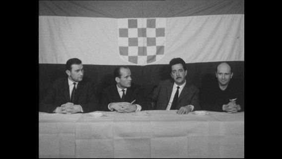 Vier Männer sitzen vor einer kroatischen Flagge.  