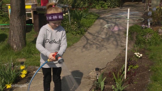 A girl waters flowers in a flower bed with a garden hose.  