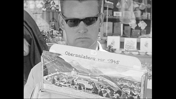 Tourist schaut Postkarte mit Aufrschrift "Obersalzberg vor 1945" an.  