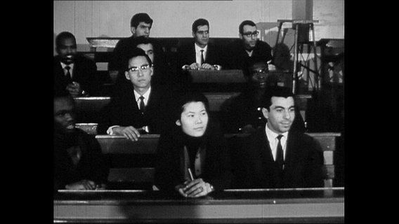 Studierende sitzen in den Reihen eines Hörsaals.  
