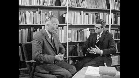 Reporter und Prof. Speer sitzen vor einem Bücherregal.  