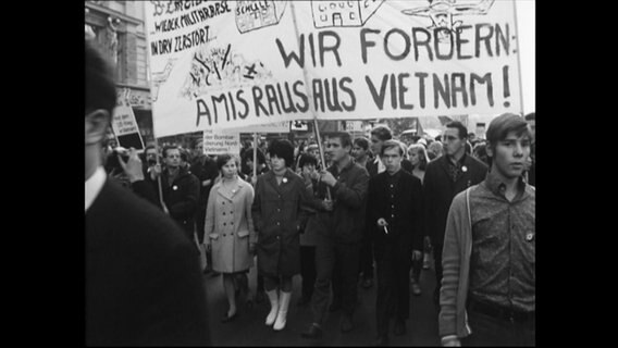 Menschen protestieren und halten das Banner "Wir fordern Amis raus aus Vietnam" hoch.  