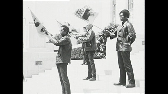 Mitglieder der Black Panthers-Bewegung stehen auf einer Treppe und schwenken Fahnen  