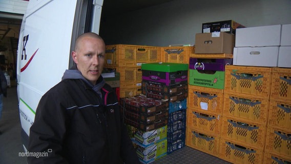 A man in front of a van packed with crates of groceries.  