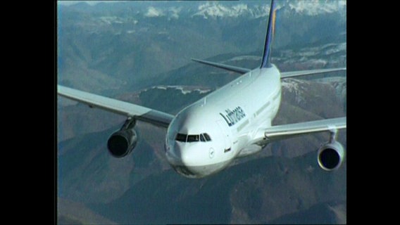 Eins Passagiermaschine in der Luft vor einem Gebirgspanorama  