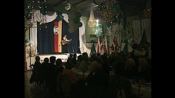 Auf der Bühne einer NPD-Veranstaltung steht ein Mann mit einer Gitarre und singt.  