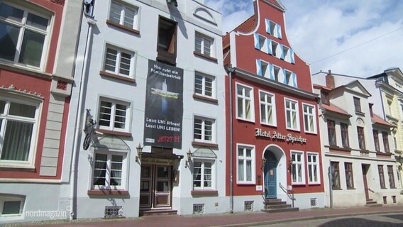 The gable house of the Hotel Alter Speicher in Wismar from the outside, a large banner calls for openings in the corona pandemic.  