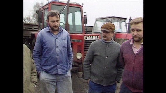 Drei LPG-Bauern stehen vor roten Traktoren (Archivbild).  
