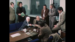 Männer sitzen und stehen um einen Tisch und beraten sich über Fahndungsfotos (Archivbild).  