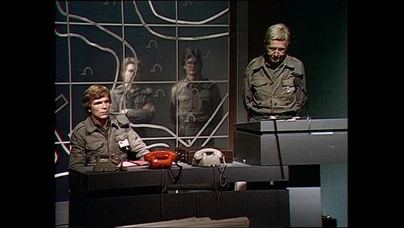 Schauspieler in militärischer Uniform stehen hinter einem Schreibtisch (Archivbild).  