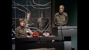 Schauspieler in militärischer Uniform stehen hinter einem Schreibtisch (Archivbild).  