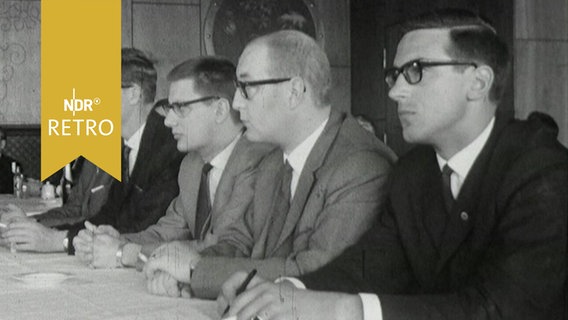 Fünf Finanzexperten hintereinander an einem Tisch bei einer Tagung 1965  
