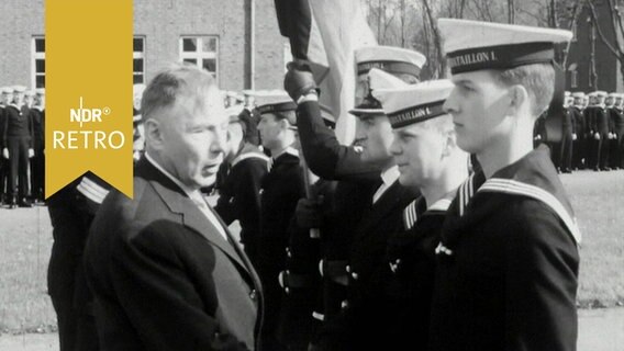 Ministerpräsident Helmut Lemke redet mit einem jungen Rekruten, sieht aber ganz woanders hin (1964)  
