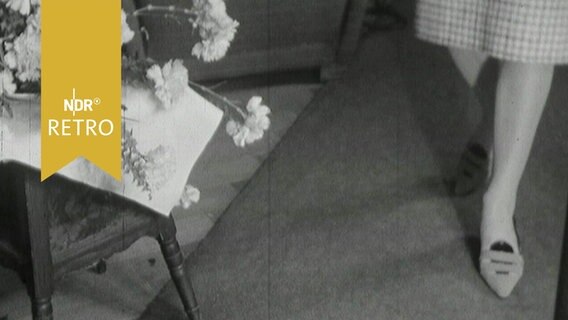 Schuh der neuen Kollektion 1964 wird von einem Mannequin präsentiert, daneben Blumen auf dem Tisch  