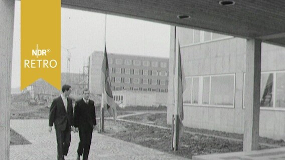 Zwei Männer auf dem Weg in ein Gebäude, im Hintergrund Neubauten der Bergakademie Clausthal (1963)  