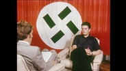 Ein Neonazi vor einer verfremdeten Hakenkreuz-Flagge  