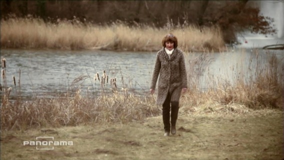 Eine Frau spaziert alleine am Ufer eines Flusses  