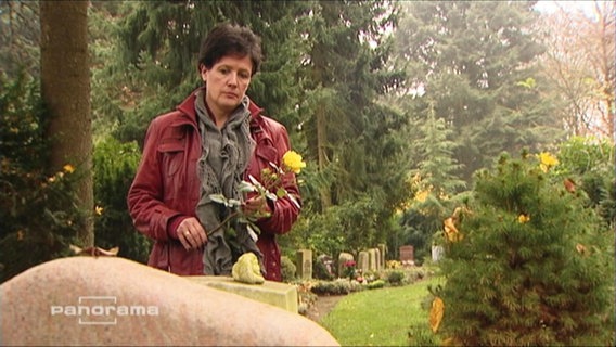 Eine Frau legt eine Rose auf ein Grab  