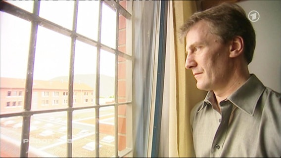Ein Mann schaut durch ein vergittertes Fenster  