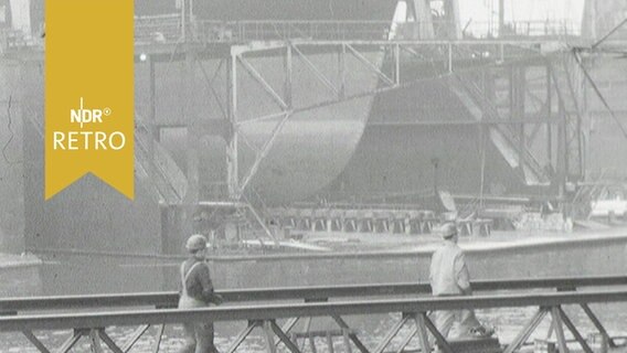 Die "Esso Bayern" im Dock der Howaldtswerke Werft in Hamburg, davor gehen zwei Arbeiter über eine Seebrücke (1964)  