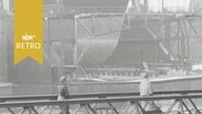Die "Esso Bayern" im Dock der Howaldtswerke Werft in Hamburg, davor gehen zwei Arbeiter über eine Seebrücke (1964)  