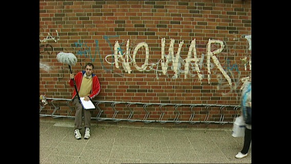 Alfons neben einem Graffiti gegn Krieg  